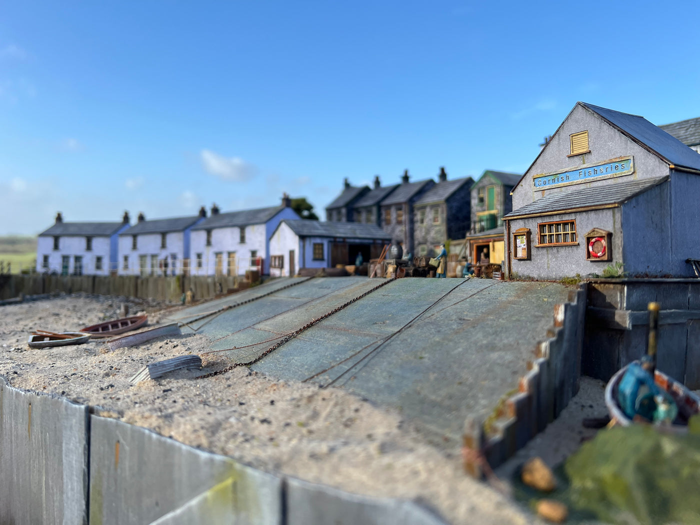 OO gauge model of a 1920s coastal village with buildings and a dock under a clear blue sky.